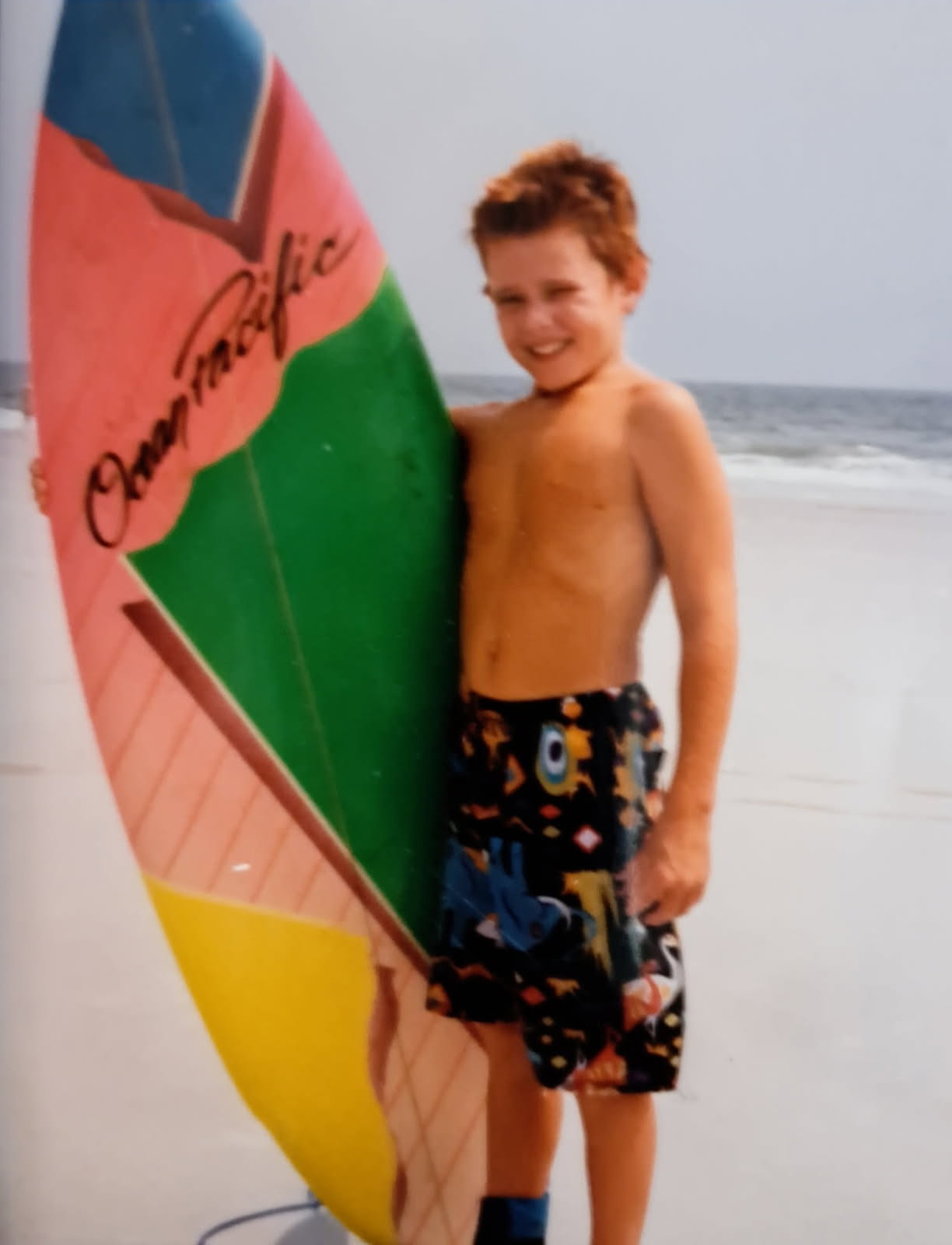 Dannon as a young boy holding a surfboard on the beach